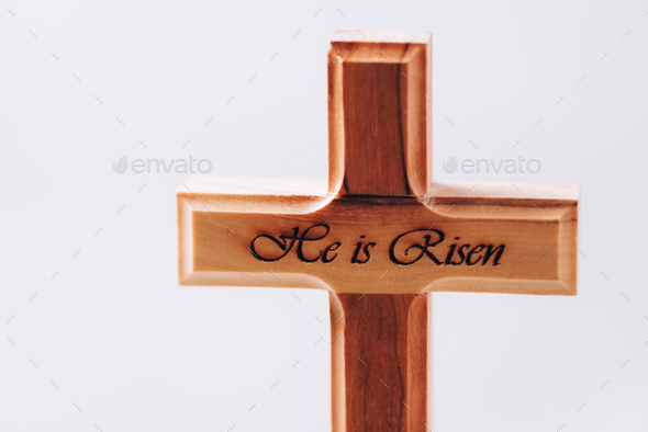 Wooden cross with text He is risen on grey background. Reminder of Jesus sacrifice and Christ