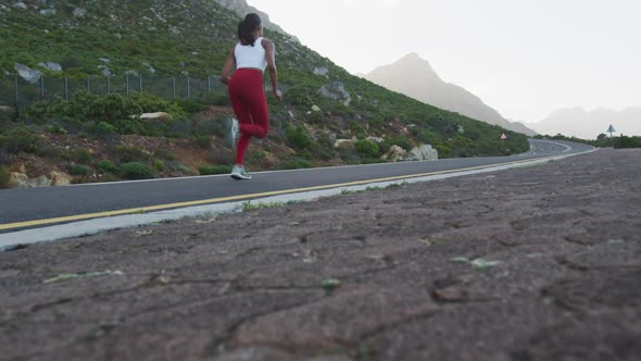 Fit mixed race woman exercising running on a country road near mountains alt