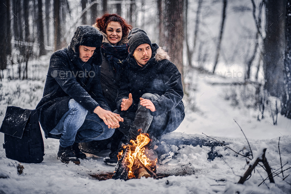 A group of friends warmed sitting by the fire in the middle of the woods