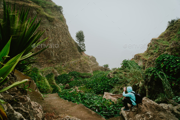 Male hiker walking through a wondrous misty landscape. Huge rocks surround a fertile ravine full of