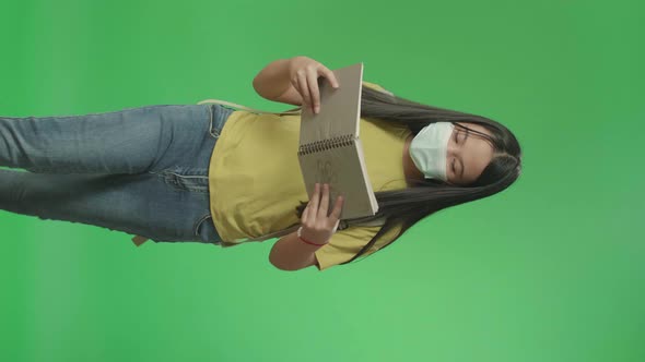 Asian Girl Student Wearing A Mask, Holding And Looking Book While Walking To School On Green Screen alt
