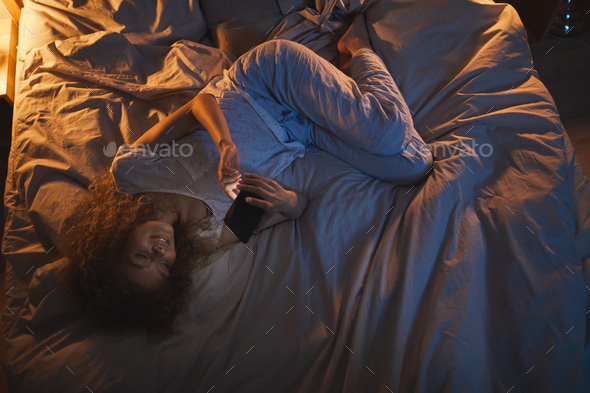 Smiling Teenage Girl using Smartphone while Lying in Bed