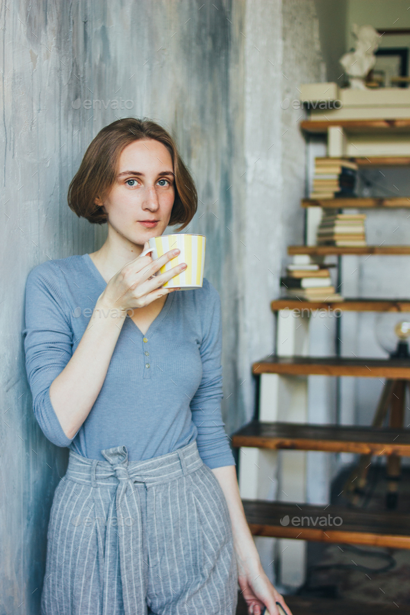 Young woman in with yellow cup standing against wall in art work studio
