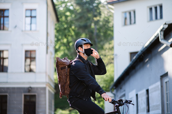 Delivery man courier on bicycle with face mask and smartphone delivering in town