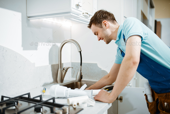 Male plumber in uniform fixing problem with faucet - Stock Photo - Images