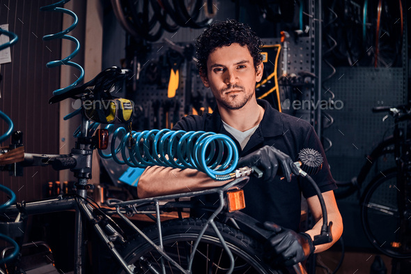 Handsome talented master is fixing bicycle at his own workshop using pneumatic tool