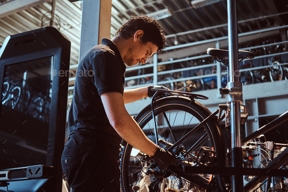 Attractive mechanic is fixing customer\'s bicycle at his own workshop.