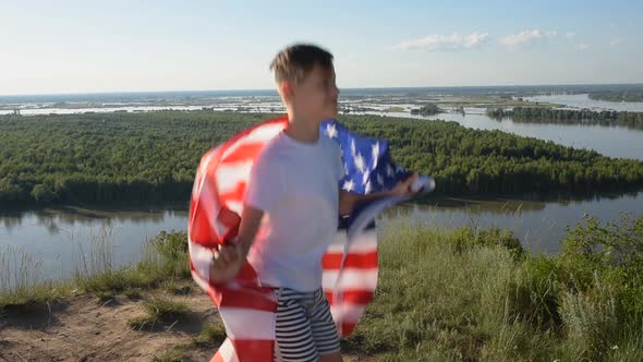 Boy Waving National USA Flag Outdoors Over Blue Sky at the River Bank