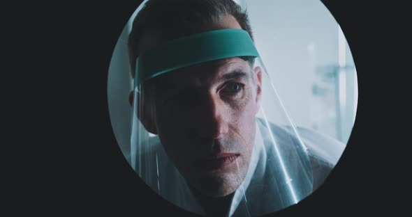 A doctor looking in a laboratory window and consulting a colleague alt