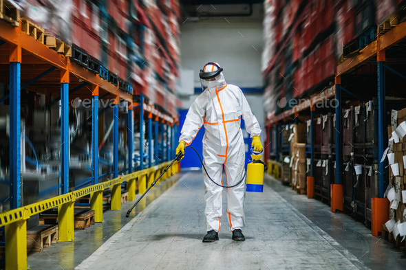 Man worker with protective mask and suit disinfecting industrial factory with spray gun