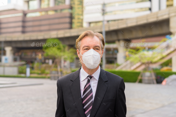 Mature businessman thinking with mask for protection from corona virus outbreak in the city outdoors