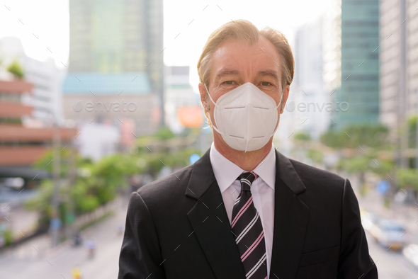 Face of mature businessman with mask for protection from corona virus outbreak against view of the