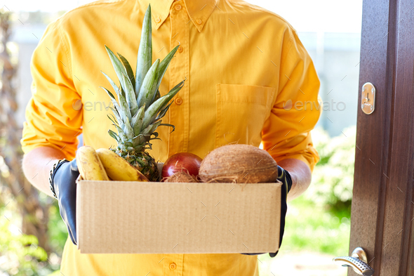 Courier man delivery box with exotic fruits food, contactless delivery.