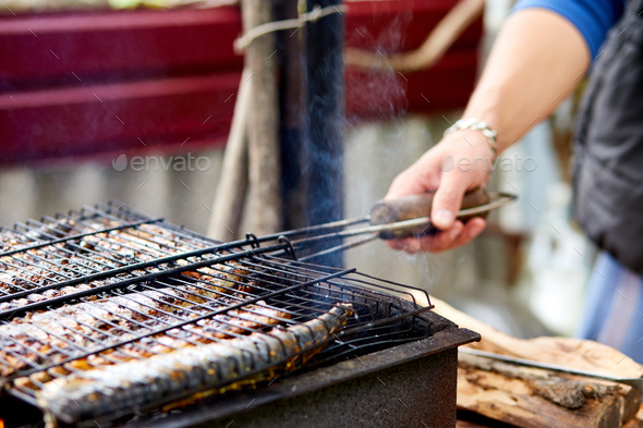 Men grilling fish mackerel on barbecue cooked on the grill in the open air flow