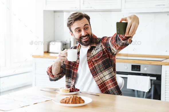 Portrait of smiling man taking selfie on cellphone and drinking coffee