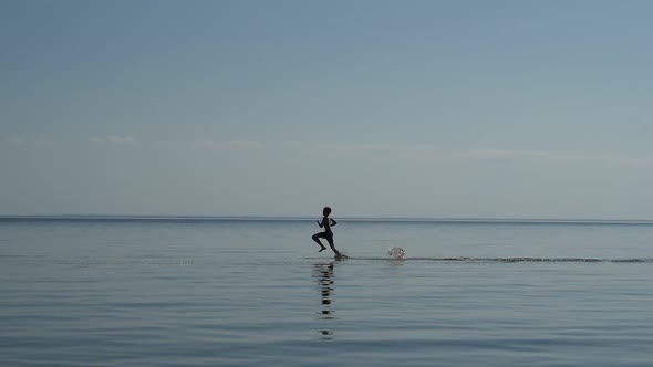 Silhouette of Two Boys Running Along the Beach on Sea Water