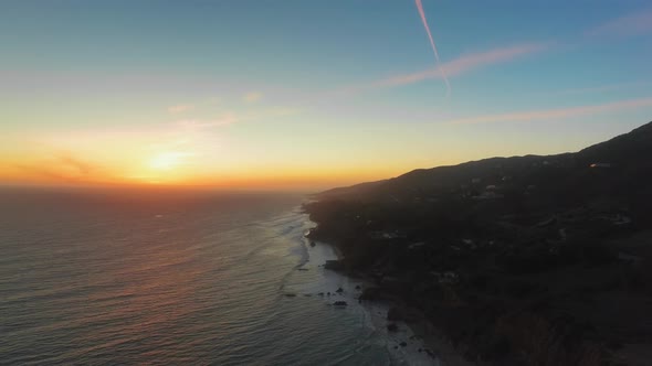Drone footage of bright sunrise over the ocean shore at El Matador Beach, Malibu, Califronia, USA  alt