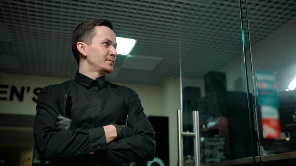 Male Barber with Crossed Arms Standing in Front of Barbershop Glass Doors alt