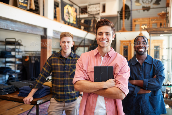 Portrait Of Smiling Multi-Cultural Male Sales Team In Fashion Store In Front Of Clothing Display