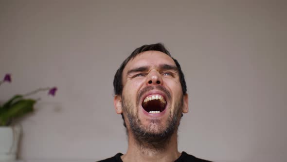 Close-up of a handsome man in a black sweatshirt laughing with his mouth wide open alt