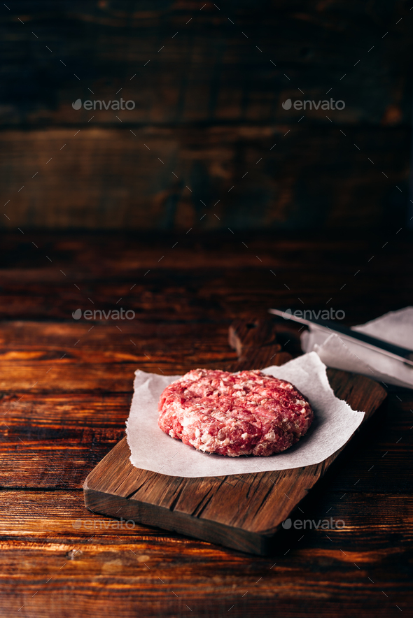 Raw beef patty for burger on cutting board - Stock Photo - Images