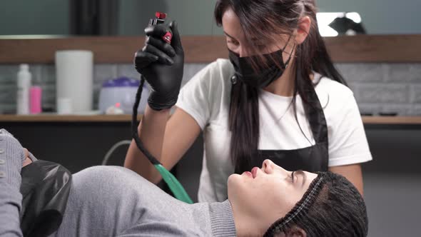 Cosmetologist Applies a Permanent Makeup to the Lips of a Caucasian Client with a Needle with a alt