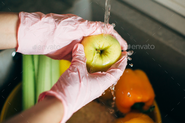 Washing fruits. Hands in pink gloves washing apple in water stream