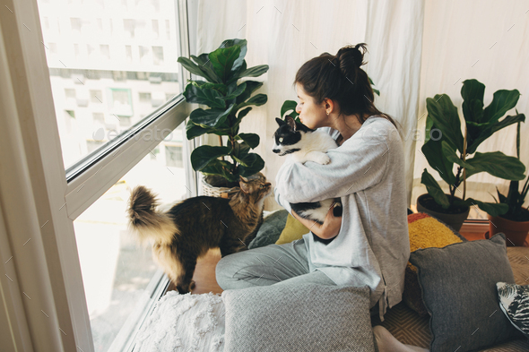 Hipster girl hugging and playing with two cats in modern room