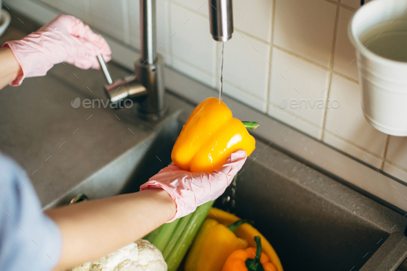 Hands in gloves washing pepper under water stream - Stock Photo - Images