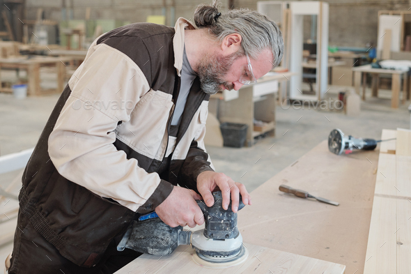 Mature worker of furniture producing factory smoothing surface of workpiece - Stock Photo - Images