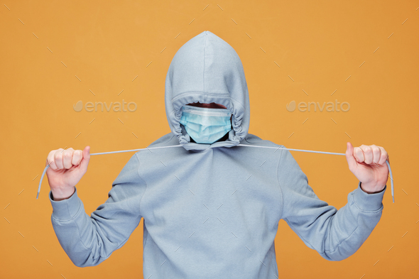 Contemporary young man in hoodie and protective mask stretching cords - Stock Photo - Images