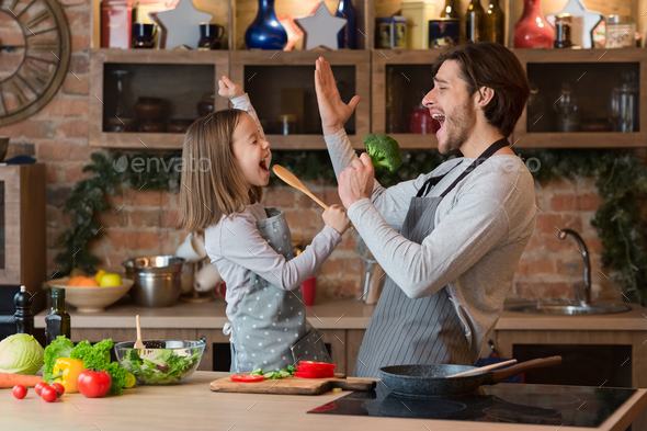 Little girl and her dad having fun in kitchen while cooking together