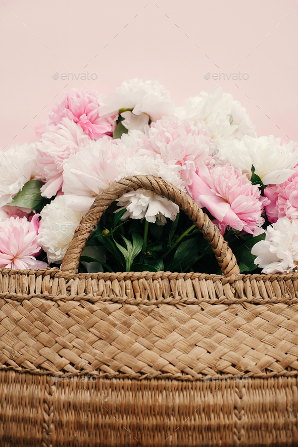Stylish straw rustic bag with white and pink peonies on pastel pink paper - Stock Photo - Images