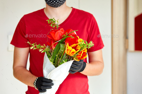 Courier, delivery man in medical latex gloves safely delivers online purchases a bouquet of flower - Stock Photo - Images