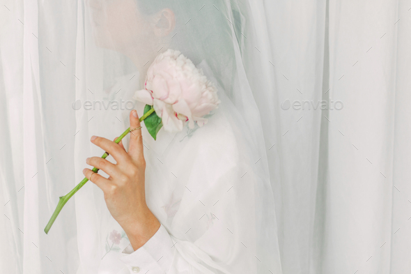 Aesthetic sensual image of beautiful woman holding pink peony flower through tulle - Stock Photo - Images