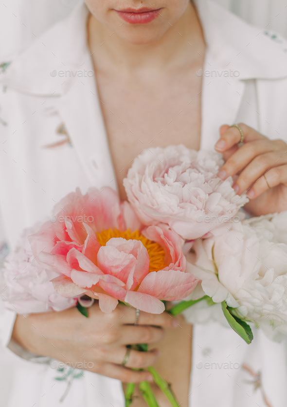 Stylish girl in white floral shirt gently holding peonies flowers in hands - Stock Photo - Images