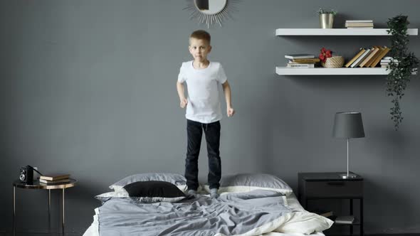 a happy little boy in pajamas jumps on his parents bed in the morning. A happy childhood for kids alt