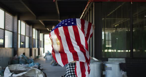 Mixed race woman holding us flag running through an empty building alt