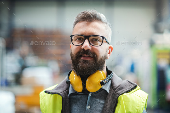 Technician or engineer with protective headphones standing in industrial factory
