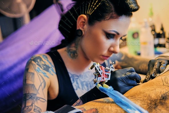 Close up image of female tattoo artist makes a tattoo on a man\'s torso.