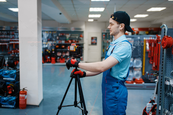 Worker testing laser level on tripod in tool store - Stock Photo - Images
