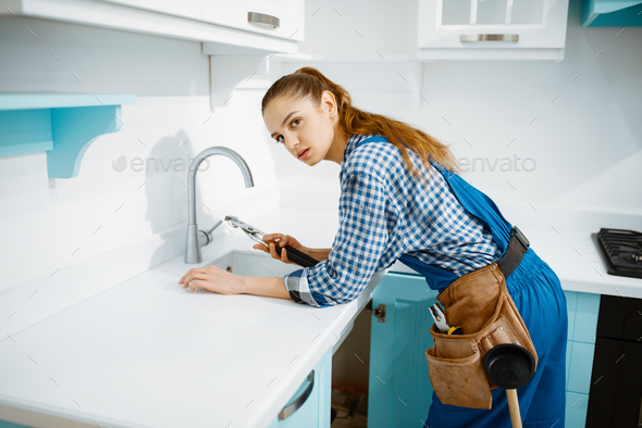 Cute female plumber in uniform fixing faucet - Stock Photo - Images