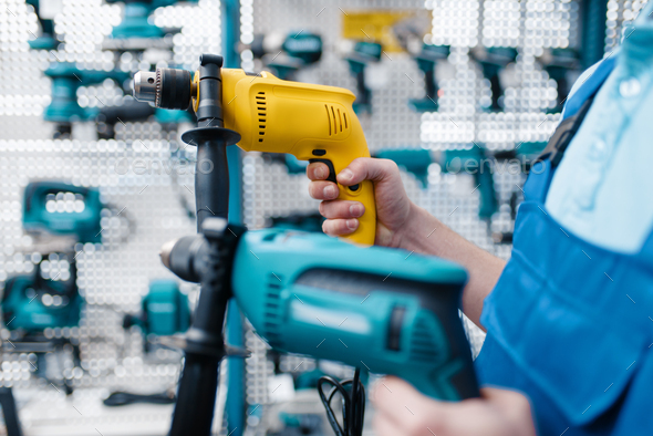 Worker holds two electric drills in tool store - Stock Photo - Images