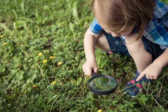 Happy little boy exploring nature with magnifying glass at the day time - Stock Photo - Images