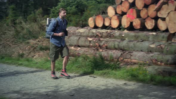 Hiker walking on hiking trail along stack of wood alt