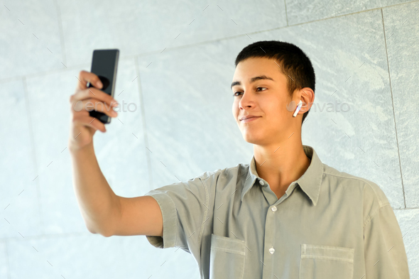 Young man wearing an earbud taking a selfie - Stock Photo - Images