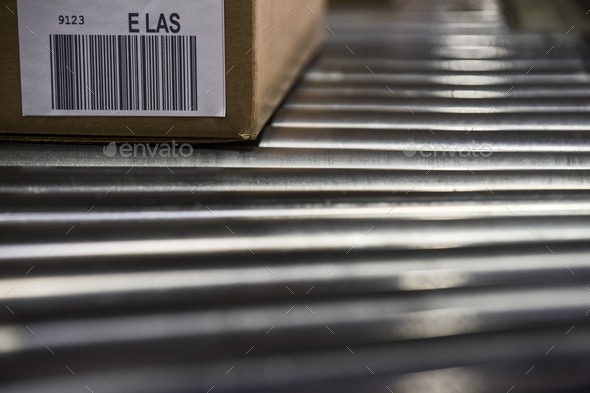Close up of shipping labels with bar codes on cardboard boxes sitting on a motorized conveyor roller