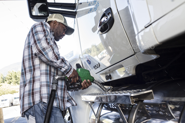 Black man truck driver putting diesel fuel in his truck at a truck stop.