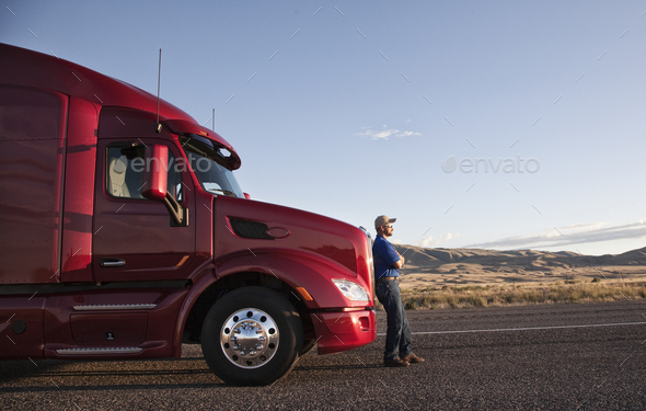 Truck driver leaning on the grill of his commercial truck. - Stock Photo - Images