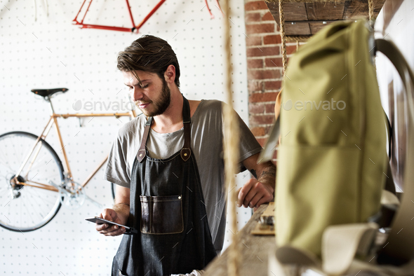 A man working in a bicycle repair shop looking at his smart phone.